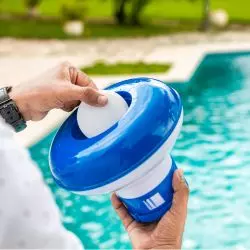 Dos manos sosteniendo un dosificador flotante de cloro junto a una piscina, categor&iacute;a tratamiento de agua